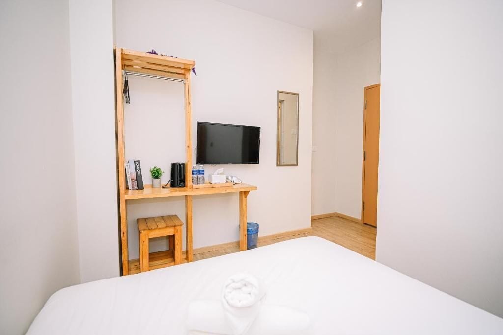 A hotel room with a bed, a wooden desk, a television, a mirror, and a door.