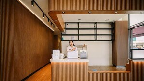 Un comptoir d’accueil avec un revêtement en bois, une personne derrière, et un aménagement intérieur moderne avec des panneaux de bois et un éclairage encastré.