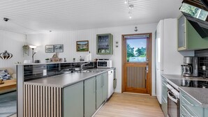 Moderni keittiö, jossa on keskeinen saareke, integroidut kodinkoneet ja näkymä ulos oven kautta.