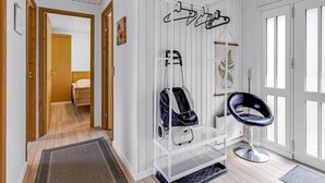 Moderni huone, jossa on valkoinen katto, metallinen vaateteline, musta tuoli ja puinen ovi, joka johtaa toiseen huoneeseen.