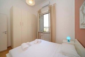 Une chambre d’hôtel comprenant un lit, une armoire, une fenêtre avec des rideaux, un radiateur et une lampe fixée au mur.