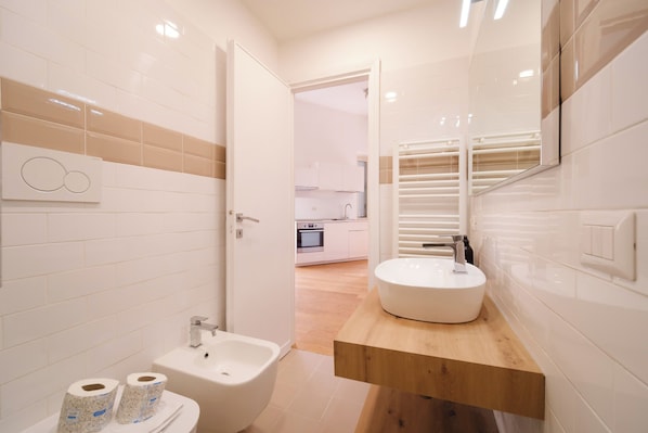 A modern bathroom with a bidet, toilet, and a sink with a wooden countertop.