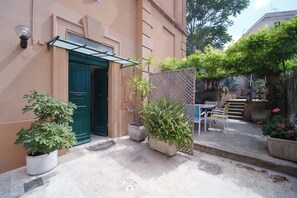 A building with a green door, potted plants, outdoor seating, and a lattice fence.