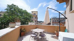 Una terraza en la azotea con mesa y sillas, plantas en macetas y una lavadora.