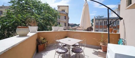A rooftop terrace with a table and chairs, potted plants, and a washing machine.