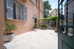 Une cour intérieure avec un bâtiment doté d’une porte verte, de plantes en pot et d’un portail en métal.