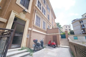 A building with a gated entrance, a red scooter parked outside, and a staircase leading to a higher level.