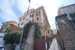 A multi-story residential building with a brick facade, a gated entrance, and a narrow alleyway.