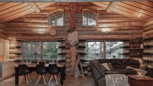A log cabin interior with a dining area, a sofa, and a large window overlooking the forest. - Villa Mörri - Cozy 4BR Cabin in Ruka (Kuusamo)