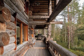 En timmerstuga med en träveranda, en grill och utsikt över skogen.