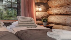 A cozy log cabin bedroom with a bed, pillows, a bedside lamp, and a window with curtains. - Villa Mörri - Cozy 4BR Cabin in Ruka (Kuusamo)
