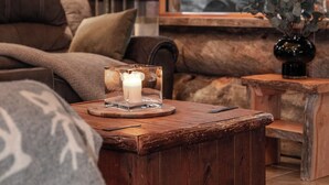 A cozy log cabin interior with a sofa, a wooden coffee table, and a window with a view of trees. - Villa Mörri - Cozy 4BR Cabin in Ruka (Kuusamo)