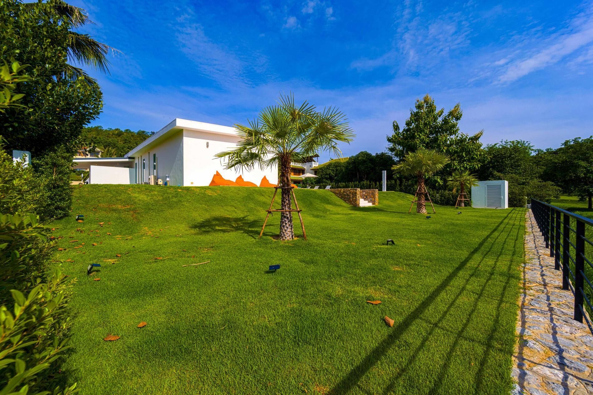 A well-maintained grassy area with a white building, palm trees, and a stone pathway.