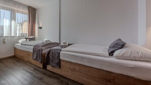 Ett modernt sovrum med en säng placerad på en träplattform, ett sängbord och ett fönster med tunna, genomskinliga gardiner.