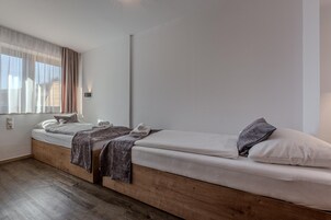 Ein modernes Schlafzimmer mit einem hölzernen Plattformbett, einem Nachttisch und einem Fenster mit transparenten Vorhängen.