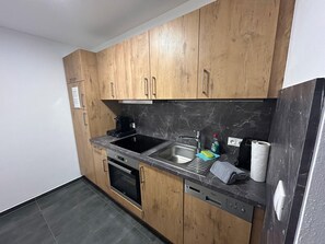 A compact kitchen with wooden cabinets, a black countertop, a stainless steel sink, a built-in oven, and a dishwasher.