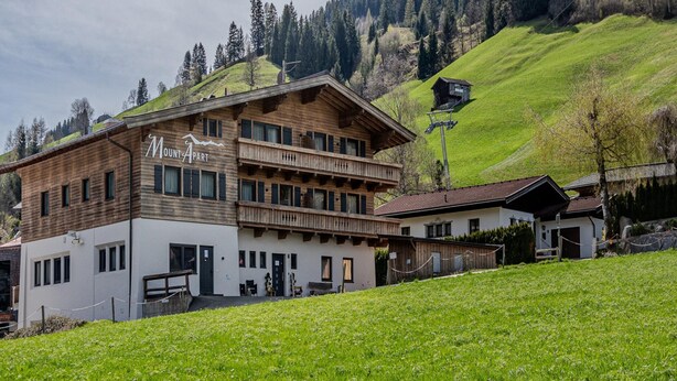 Eine Berglodge mit Holzfassade, mehreren Balkonen und Blick auf die umliegenden Hügel.