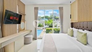 Habitación de hotel moderna con una cama grande, un televisor montado en la pared y vistas a una piscina y edificios.