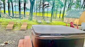 Uma banheira de hidromassagem em área arborizada, com espreguiçadeiras de madeira e uma mesa para piquenique.