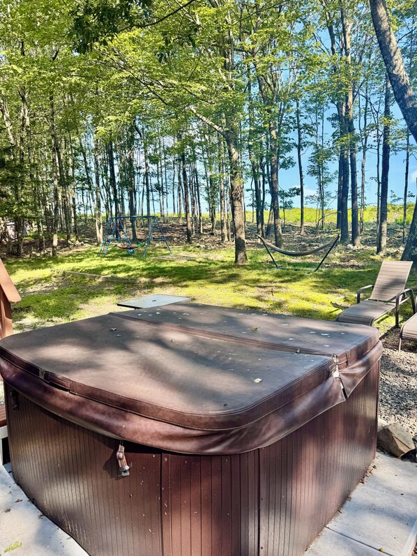A hot tub in a forested area with a swing set and a hammock.