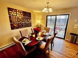 A dining area with a wooden table set for four, a chandelier, and a large window with a view of a deck.