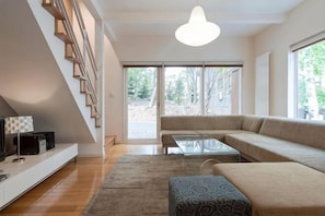 A modern living room with a sofa, a coffee table, a TV, and a staircase. - Baw Baw Sansou (Kutchan)