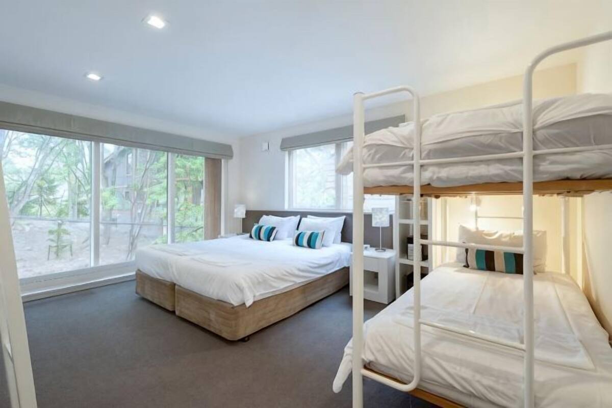 Una habitación con literas, una cama individual y un escritorio con una silla.