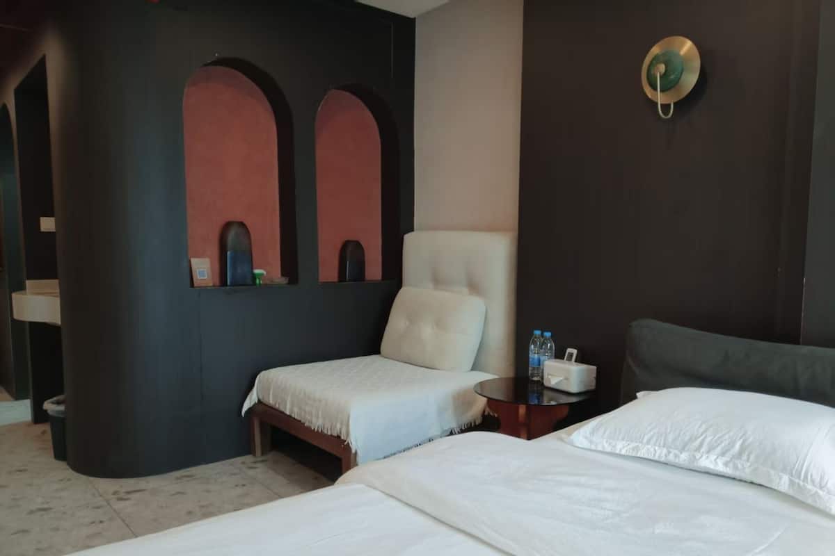 Habitación de hotel con dos camas, una mesita y una botella de agua, además de una lámpara fijada a la pared.