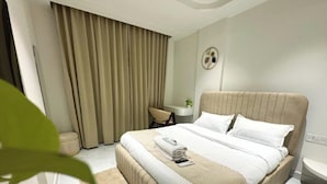 Ein Hotelzimmer mit einem großen Bett, einem Schreibtisch, einem Stuhl und einem Fenster mit Vorhängen.