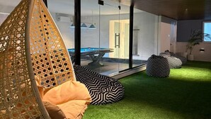 Ein modernes Interieur mit einem Hängekorbstuhl, grünem Kunstgrashalm und schwarz-weiß gemusterten Sitzsäcken.