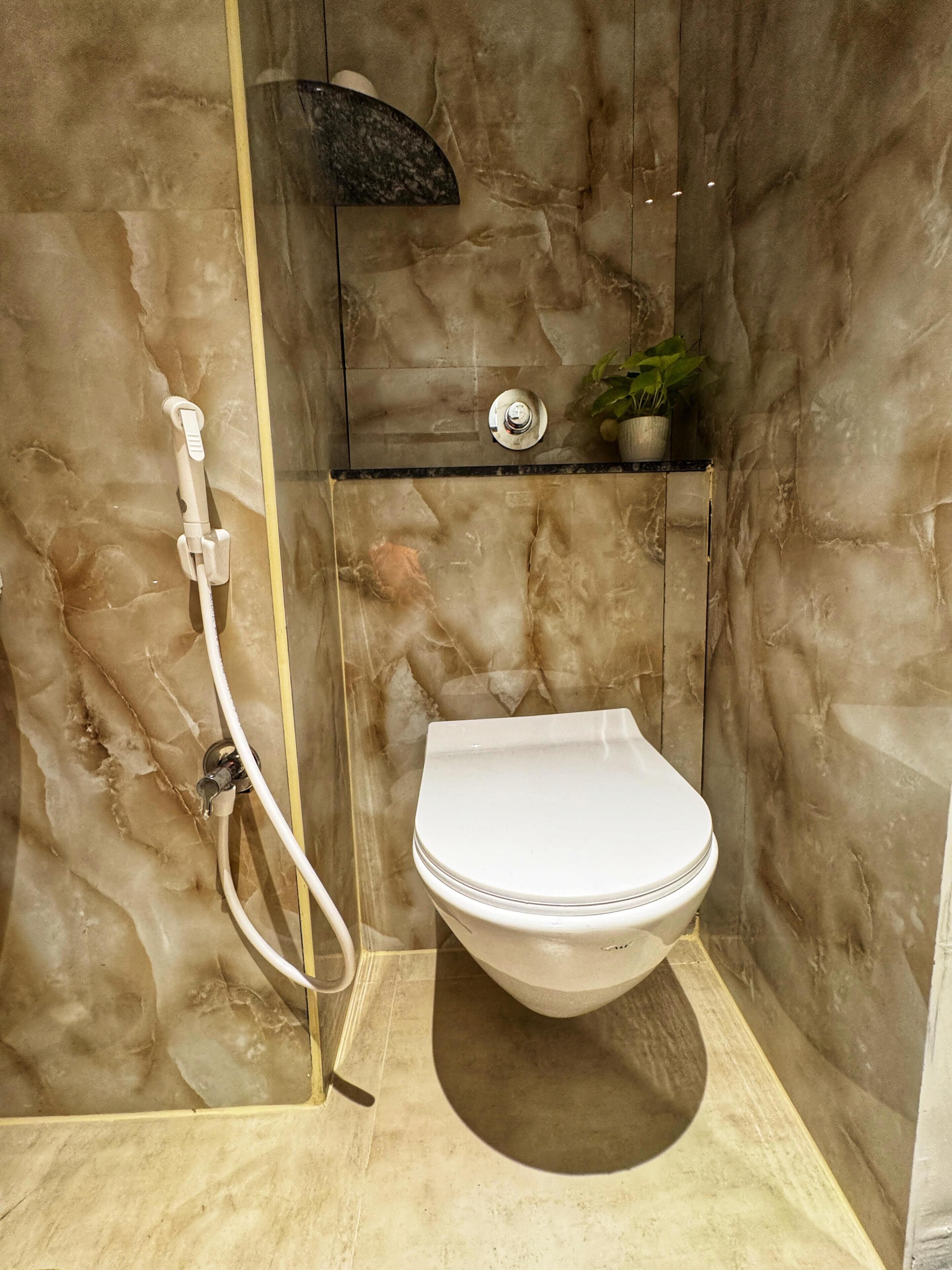 Un baño con pared de mármol, un inodoro, ducha y un estante pequeño con una planta.