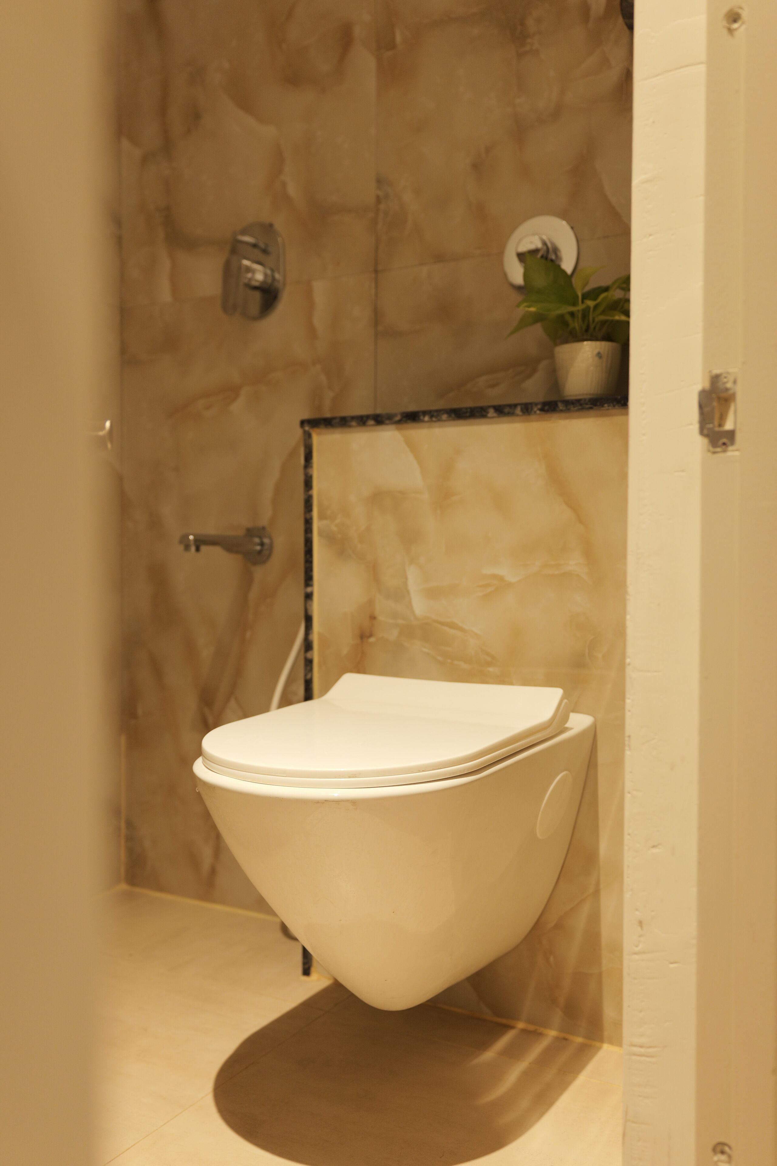 A modern bathroom with a unique, curved toilet design, a marble wall, and a small potted plant on the counter.