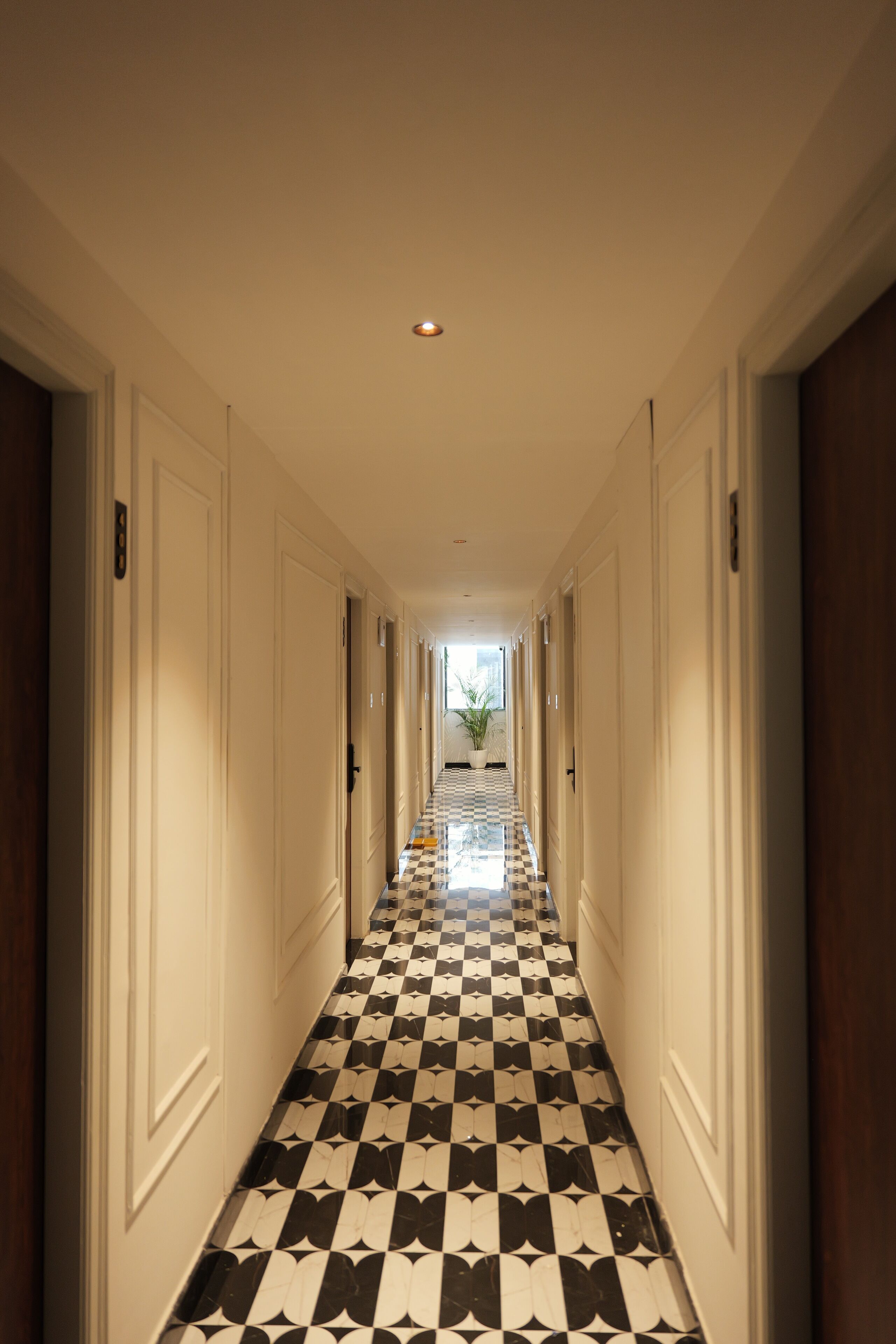 Un couloir d’hôtel avec un sol à carreaux, des murs blancs et des portes de chaque côté.
