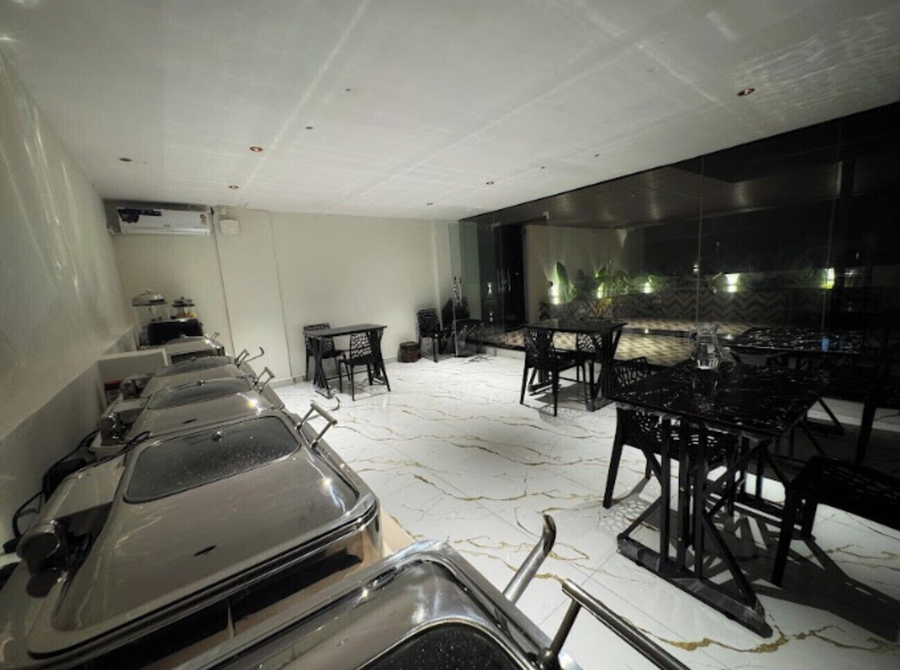 A modern dining area with a long table and chairs, a glass partition, and a view of the outside.