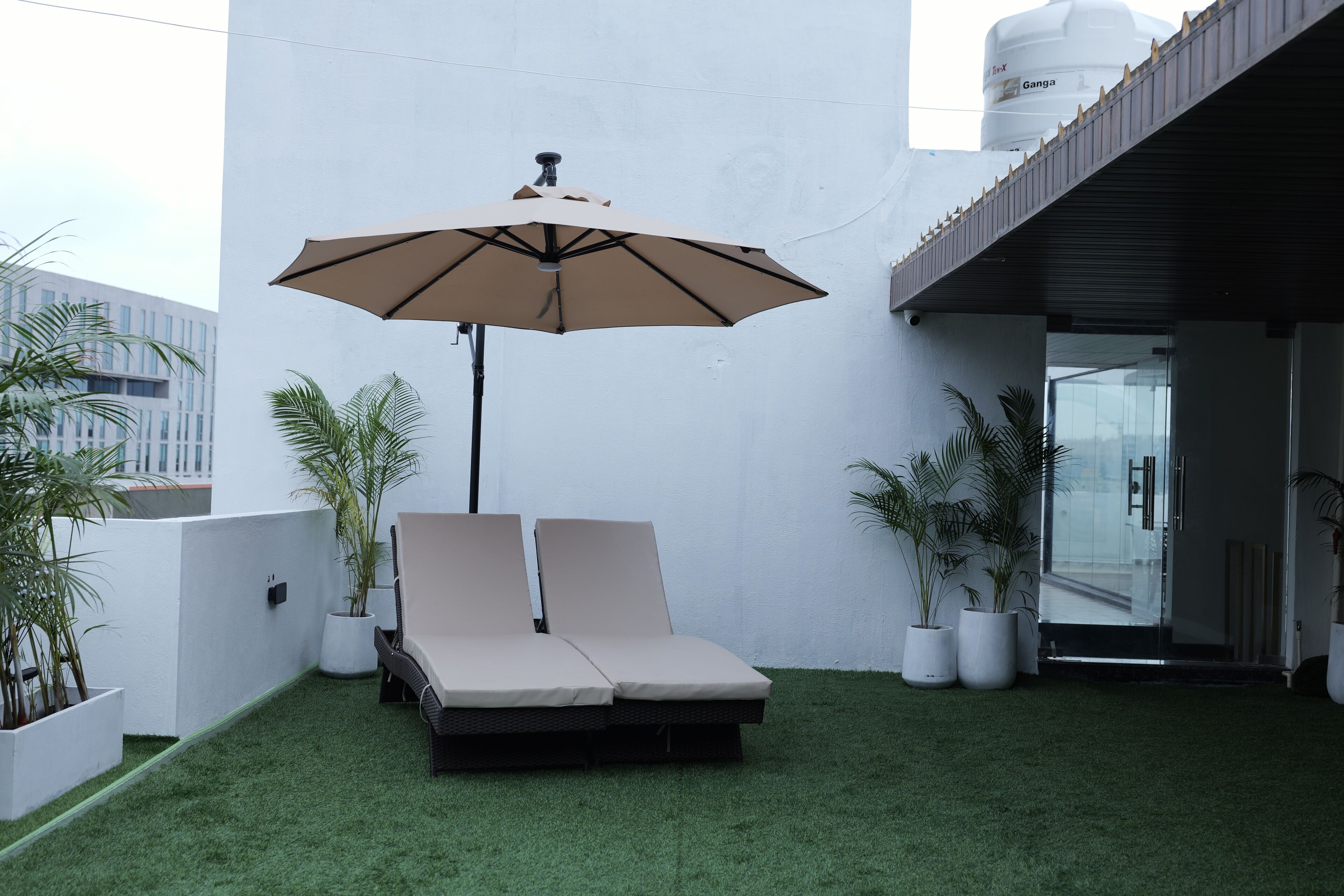 Un área de lounge en la azotea con dos sillones, una sombrilla grande y plantas en macetas.