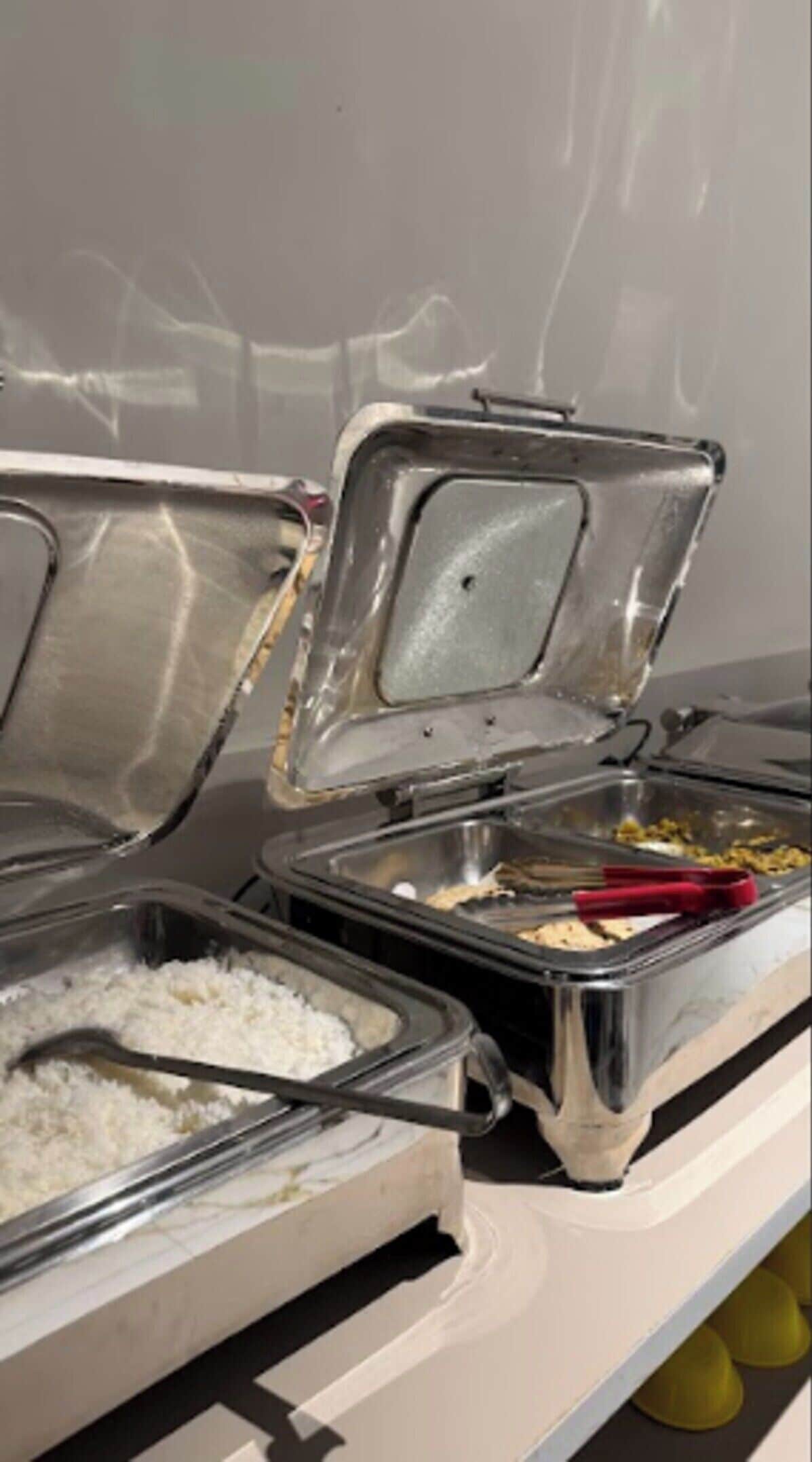 A buffet setup with various food containers, including rice and a dish with a red utensil.