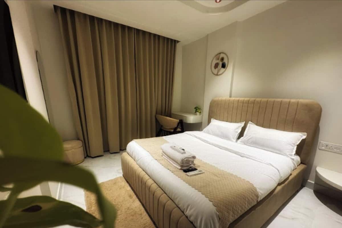 Una habitación de hotel con cama, escritorio, silla y un ventanal con cortinas.