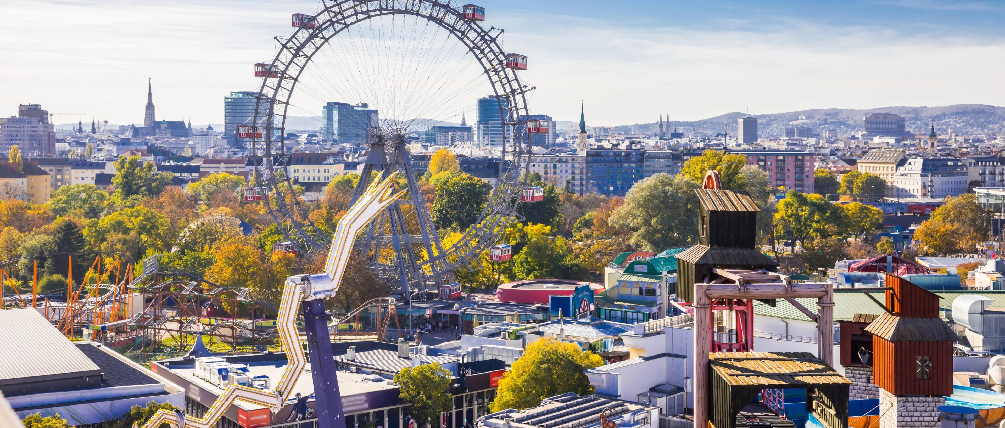 Eine Stadtansicht mit einem markanten Riesenrad, verschiedenen Gebäuden und einer Achterbahn.