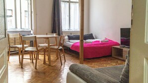 Quarto com uma cama, televisão, mesa com cadeiras e janela com cortinas.