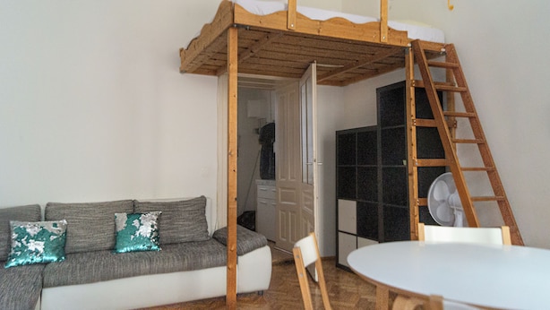 Um quarto com beliche, sofá, mesa e ventoinha.
