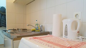 Uma cozinha com pia, uma garrafa de detergente, um dispensador de papel toalha e uma chaleira branca.