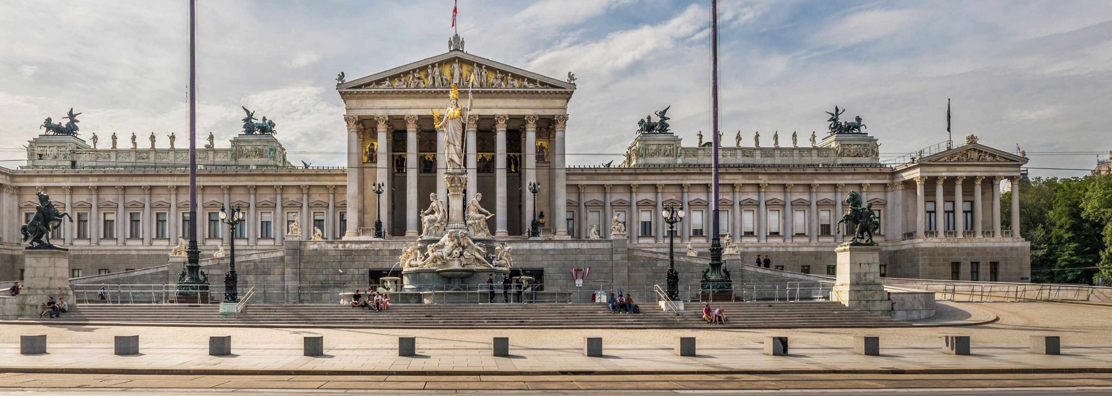 A large, classical building with a central statue and columns, surrounded by a wide plaza.