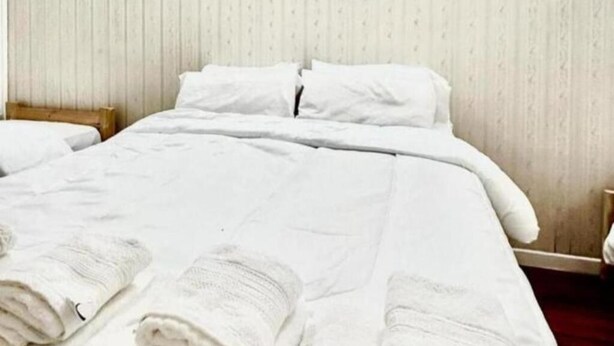 A neatly made bed with white linens and pillows, a wooden headboard, and a striped wallpaper background. - Blue hostel (Buenos Aires)
