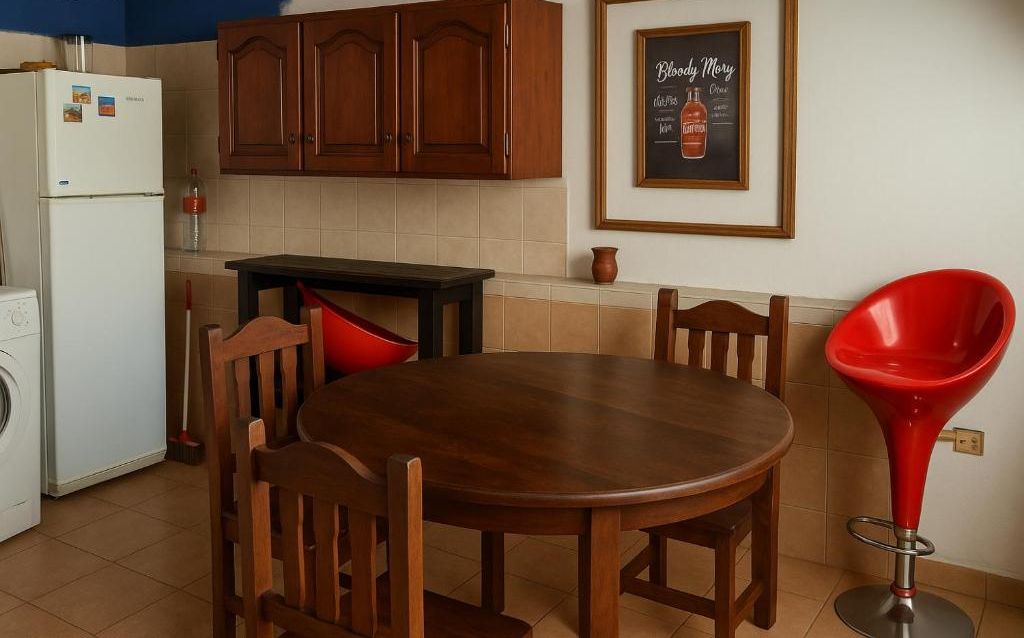 Una cocina con armarios de madera, un refrigerador blanco, una mesa de comedor con sillas y un taburete rojo.