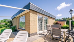 A patio area with outdoor seating, a small brick building, and a view of the garden. - Modernly Furnished 6-person Bungalow in the Seaside Resort of De Koog (De Koog)