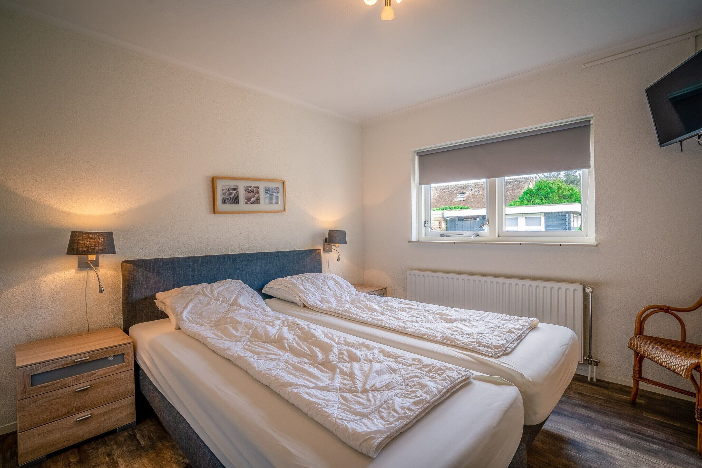 A bedroom with two beds, a nightstand, a lamp, a window, and a chair.