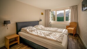 A bedroom with two beds, a nightstand, a chair, a window with curtains, and a wall-mounted TV. - Modernly Furnished 6-person Bungalow in the Seaside Resort of De Koog (De Koog)