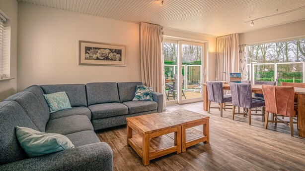 A modern living room with a sectional sofa, a wooden coffee table, and a dining area with chairs and a table. - Modernly Furnished 6-person Bungalow in the Seaside Resort of De Koog (De Koog)