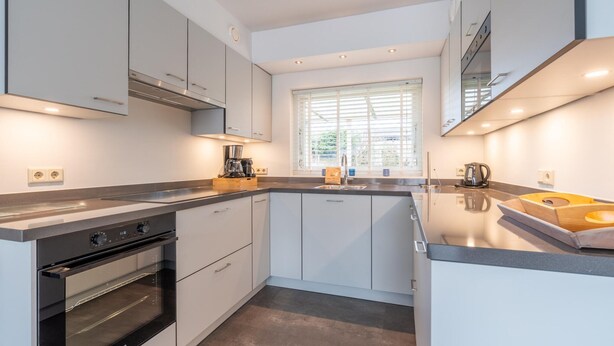 A modern kitchen with white cabinets, a built-in oven, and a large window providing natural light. - Modernly Furnished 6-person Bungalow in the Seaside Resort of De Koog (De Koog)