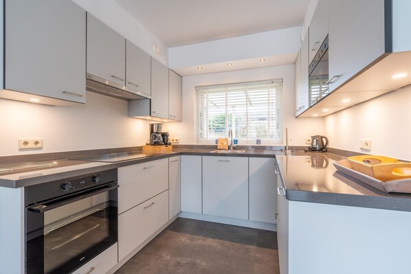 A modern kitchen with white cabinets, a built-in oven, and a large window providing natural light. - Modernly Furnished 6-person Bungalow in the Seaside Resort of De Koog (De Koog)